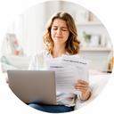 Graduate in a bright living room holding a laptop and statement documents